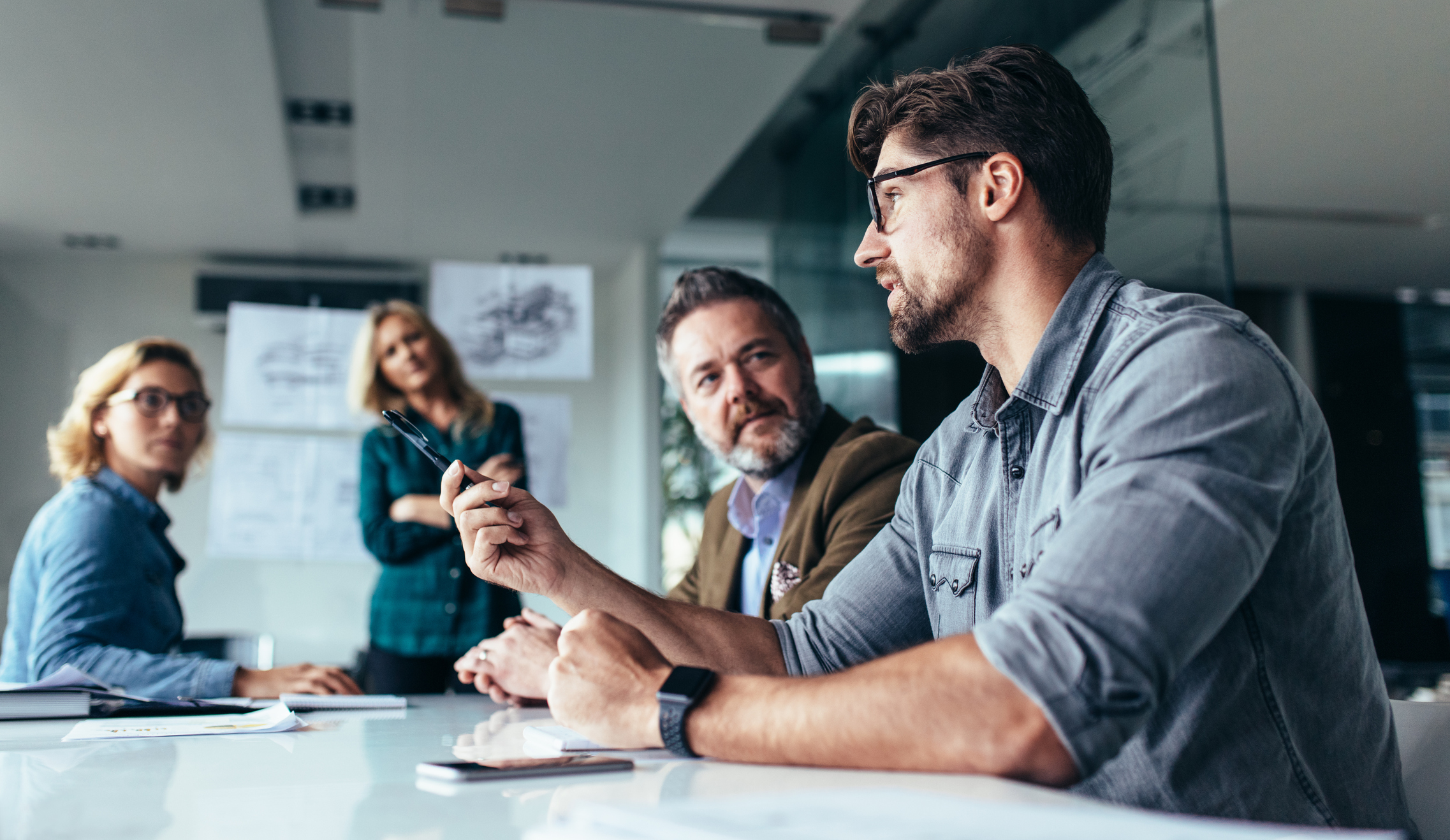 Young designer giving some new ideas about project to his partners in conference room. Business people discussing over new business project in office.